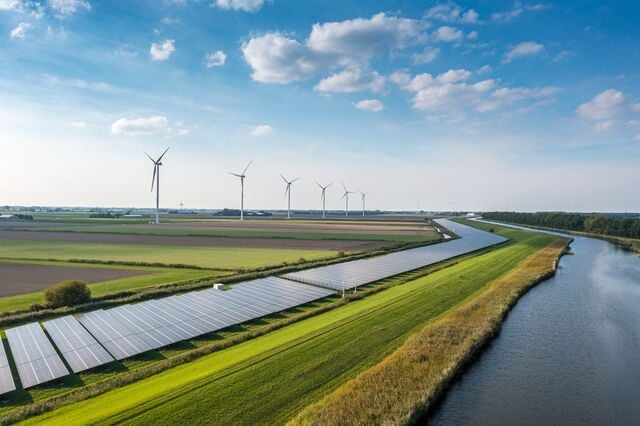 Landscape featuring solar panels and wind turbines across agricultural fields near a river, showcasing sustainable energy infrastructure and eco-friendly land use.